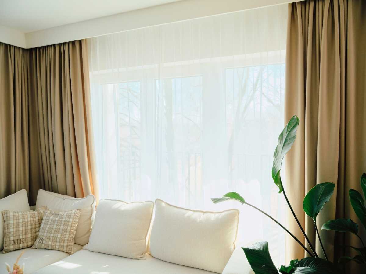 Gemütliches Wohnzimmer mit beigen Vorhängen und grüner Pflanze