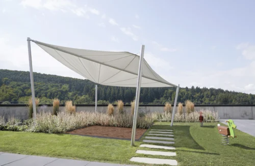 Moderne Sonnensegel über einem Spielbereich mit grüner Landschaft im Hintergrund