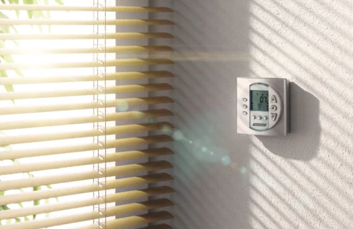 Sonnenlicht fällt durch Jalousien auf eine Wand mit einem digitalen Thermostat