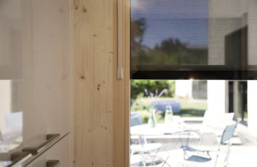 Moderner Innenraum mit Blick auf einen sonnigen Garten durch ein Fenster mit einem halb heruntergelassenen Rollladen.